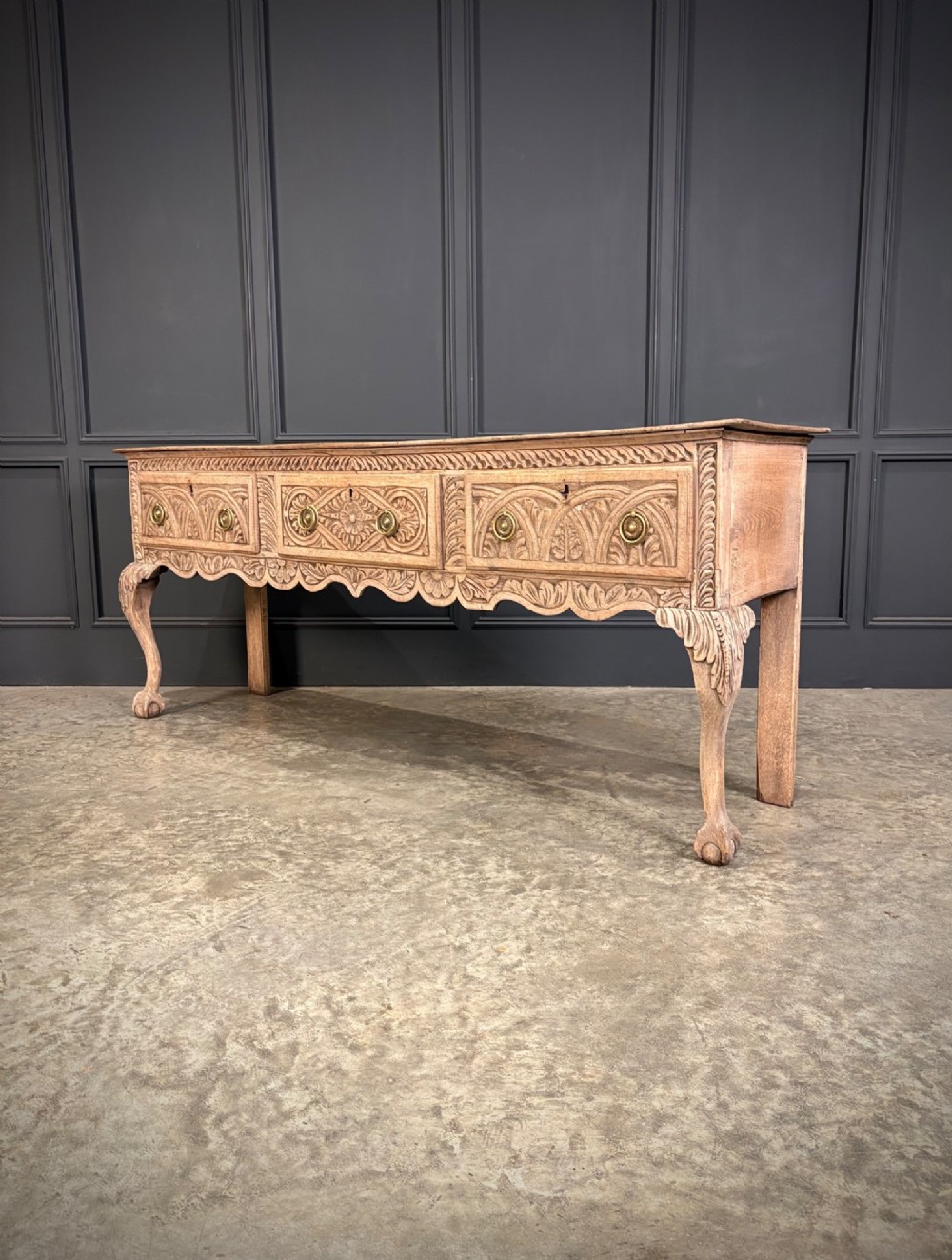 An 18th-century carved oak dresser base with three carved drawer fronts, a decorative apron, cabriole front legs, and claw and ball feet. View VIII