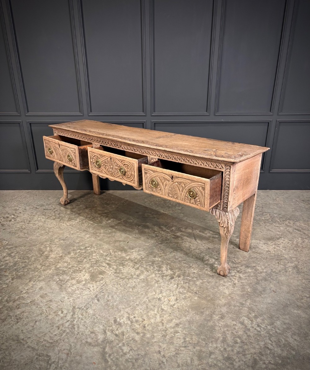 An 18th-century carved oak dresser base with three carved drawer fronts, a decorative apron, cabriole front legs, and claw and ball feet. View XII