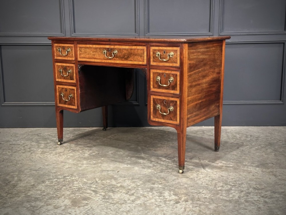 An eighteenth-century mahogany writing desk featuring a central oval floral marquetry inlay on top, crossbanded borders, seven drawers with brass handles, and square tapered legs. View II