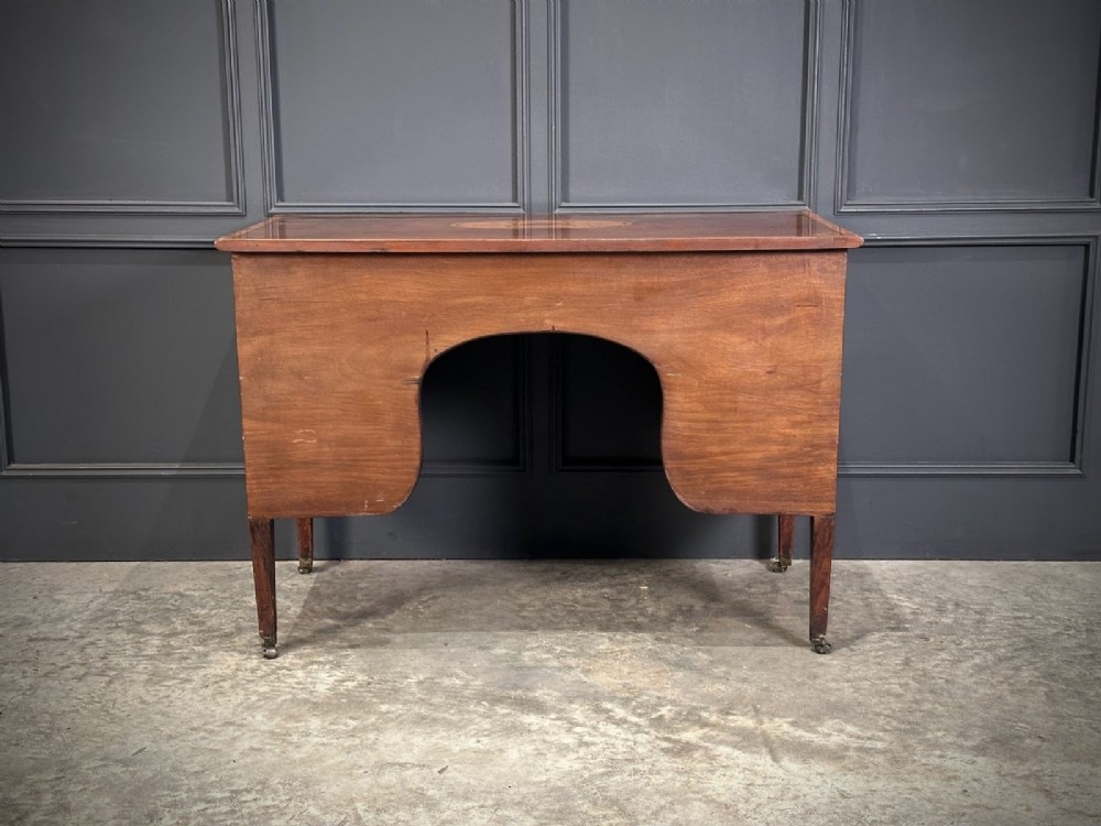 An eighteenth-century mahogany writing desk featuring a central oval floral marquetry inlay on top, crossbanded borders, seven drawers with brass handles, and square tapered legs. View IV
