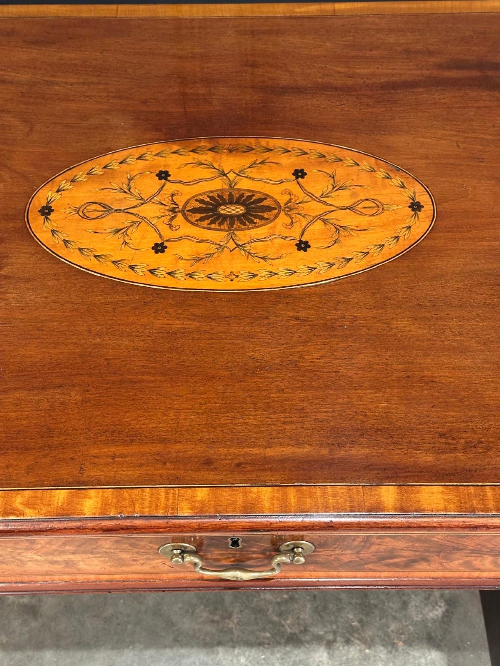 An eighteenth-century mahogany writing desk featuring a central oval floral marquetry inlay on top, crossbanded borders, seven drawers with brass handles, and square tapered legs. View V