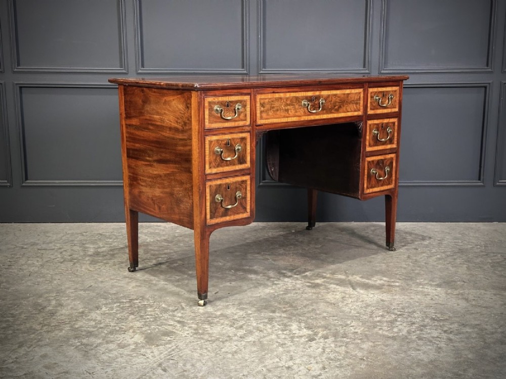 An eighteenth-century mahogany writing desk featuring a central oval floral marquetry inlay on top, crossbanded borders, seven drawers with brass handles, and square tapered legs. View VI