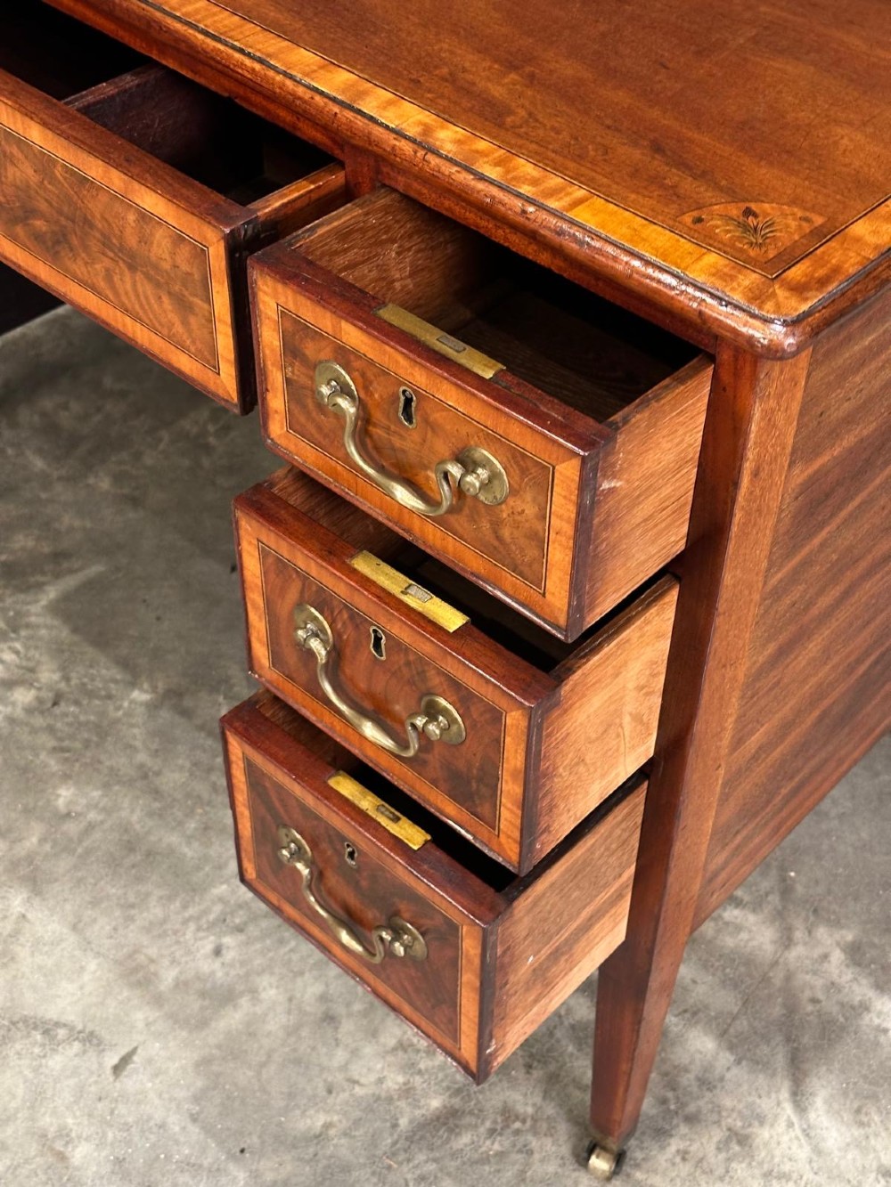 An eighteenth-century mahogany writing desk featuring a central oval floral marquetry inlay on top, crossbanded borders, seven drawers with brass handles, and square tapered legs. View X