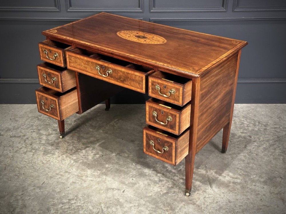An eighteenth-century mahogany writing desk featuring a central oval floral marquetry inlay on top, crossbanded borders, seven drawers with brass handles, and square tapered legs. View XI