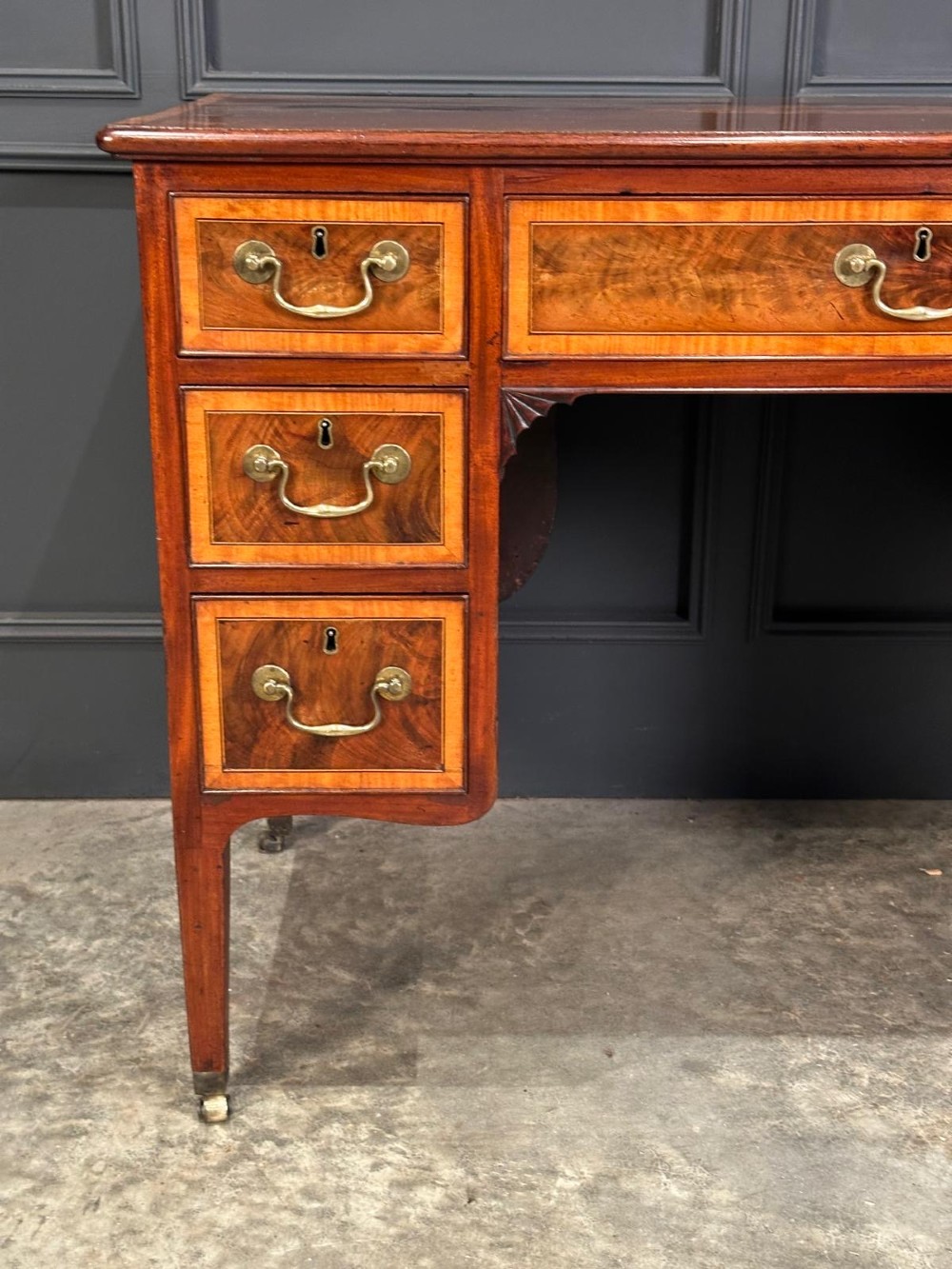 An eighteenth-century mahogany writing desk featuring a central oval floral marquetry inlay on top, crossbanded borders, seven drawers with brass handles, and square tapered legs. View XII
