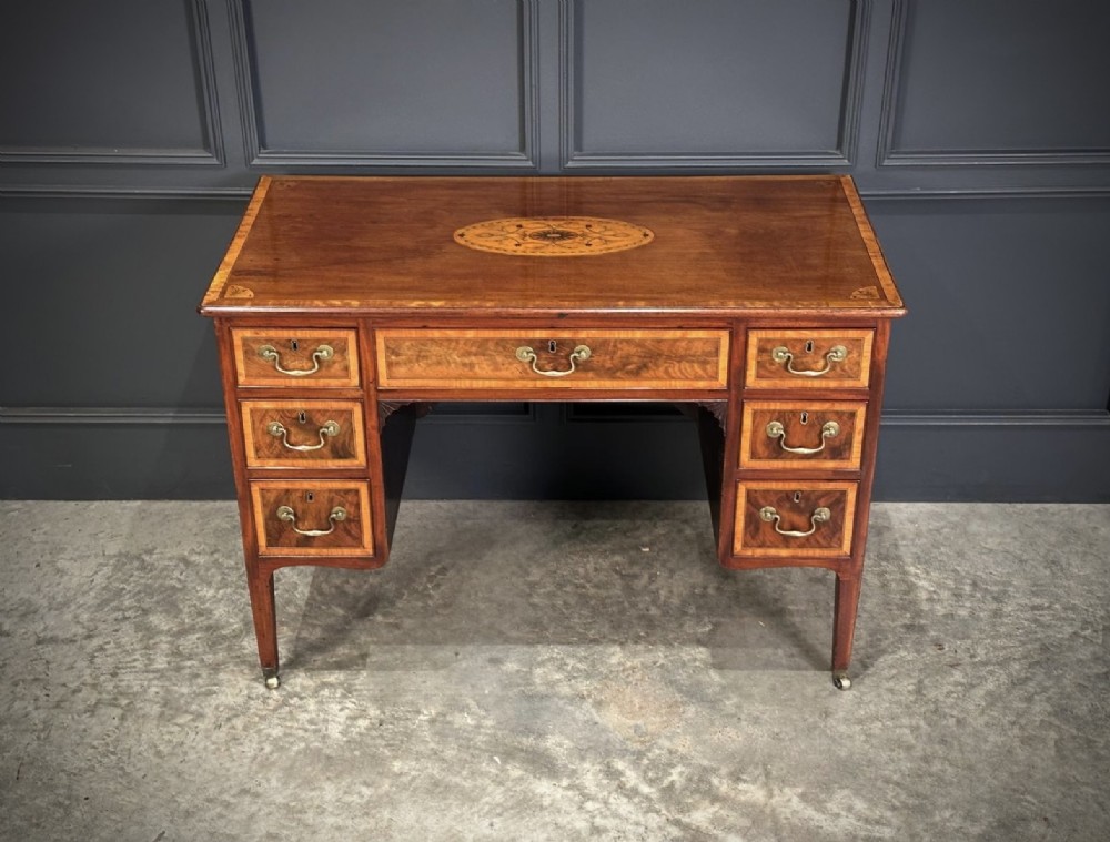 An eighteenth-century mahogany writing desk featuring a central oval floral marquetry inlay on top, crossbanded borders, seven drawers with brass handles, and square tapered legs. View XIII