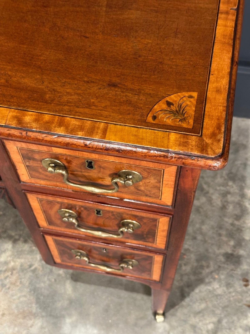 An eighteenth-century mahogany writing desk featuring a central oval floral marquetry inlay on top, crossbanded borders, seven drawers with brass handles, and square tapered legs. View XIV