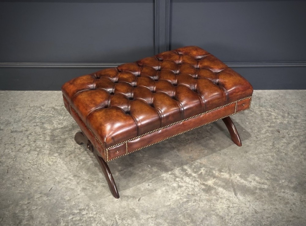 A rectangular hand-dyed brown leather footstool with deep button tufting, brass studding, and an X-frame wooden base. View III