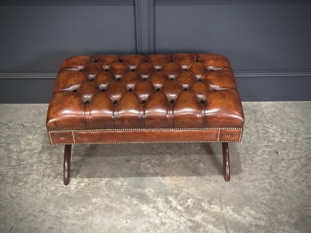 A rectangular hand-dyed brown leather footstool with deep button tufting, brass studding, and an X-frame wooden base. View IV