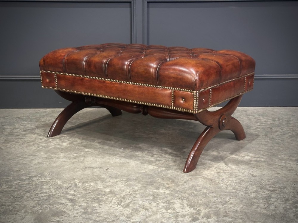 A rectangular hand-dyed brown leather footstool with deep button tufting, brass studding, and an X-frame wooden base. View IX