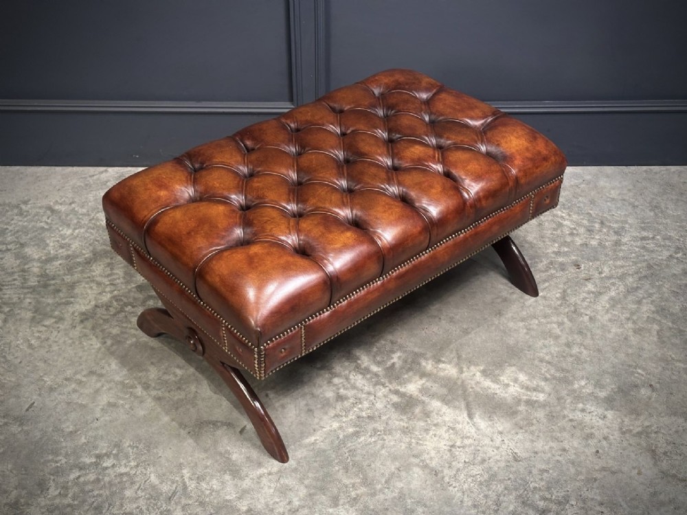 A rectangular hand-dyed brown leather footstool with deep button tufting, brass studding, and an X-frame wooden base. View XI