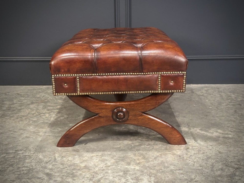 A rectangular hand-dyed brown leather footstool with deep button tufting, brass studding, and an X-frame wooden base. View XII