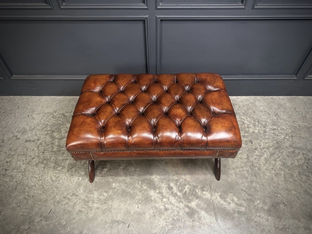 A rectangular hand-dyed brown leather footstool with deep button tufting, brass studding, and an X-frame wooden base. View XIII