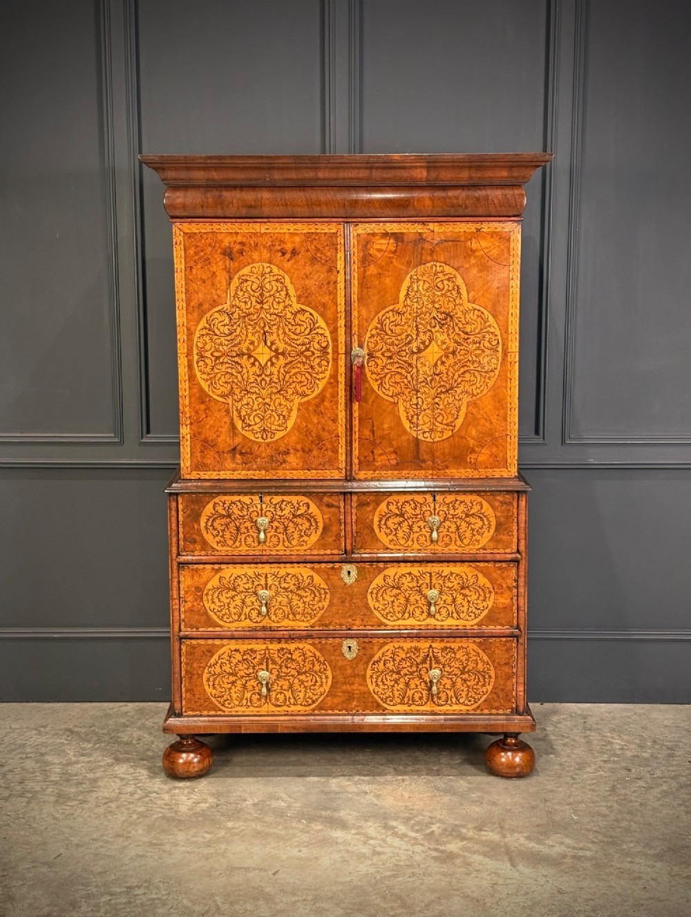 A William and Mary period burr walnut cabinet on stand featuring detailed floral marquetry inlays, teardrop brass handles, and heavy bun feet. View II