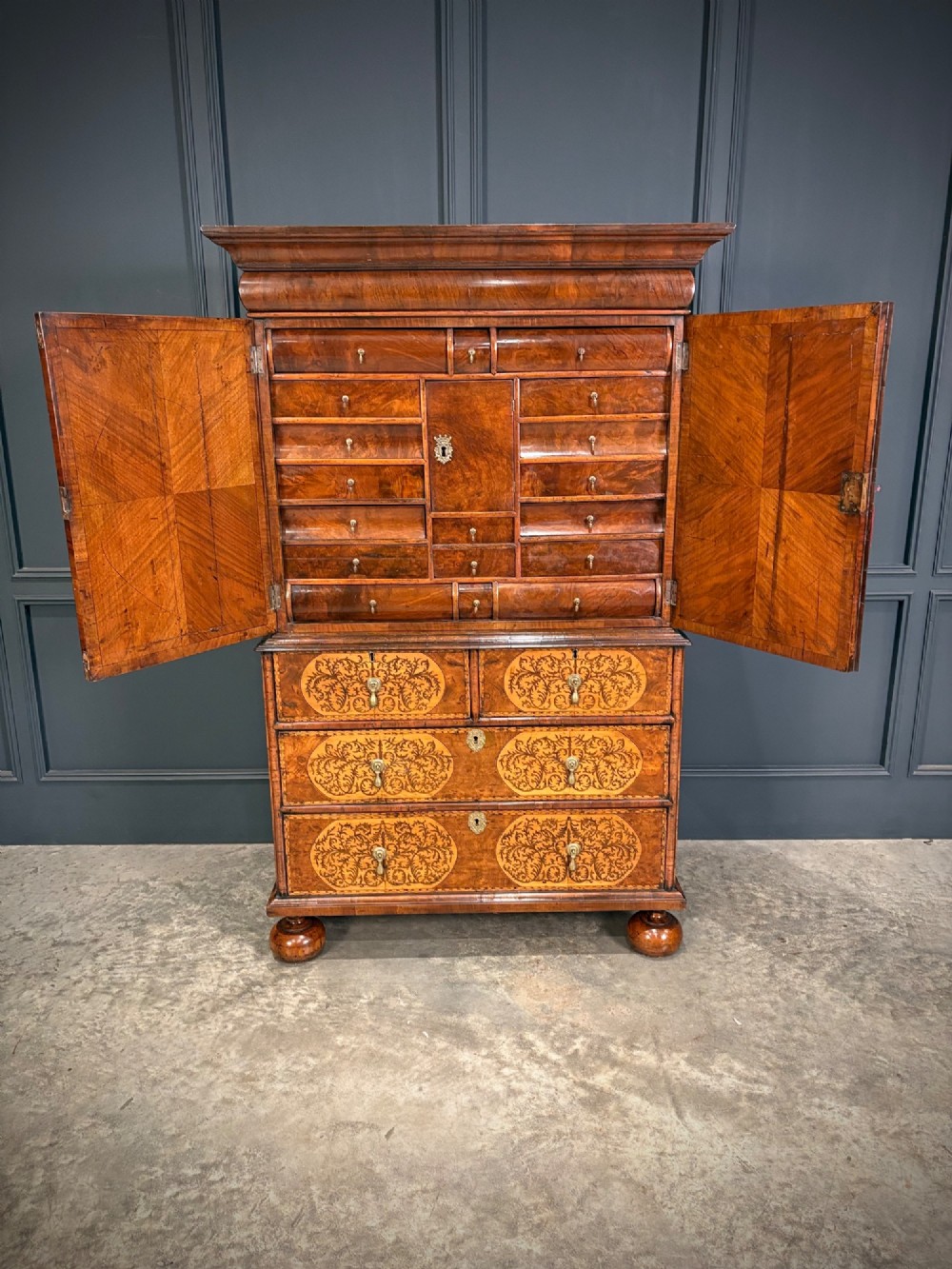 A William and Mary period burr walnut cabinet on stand featuring detailed floral marquetry inlays, teardrop brass handles, and heavy bun feet. View III
