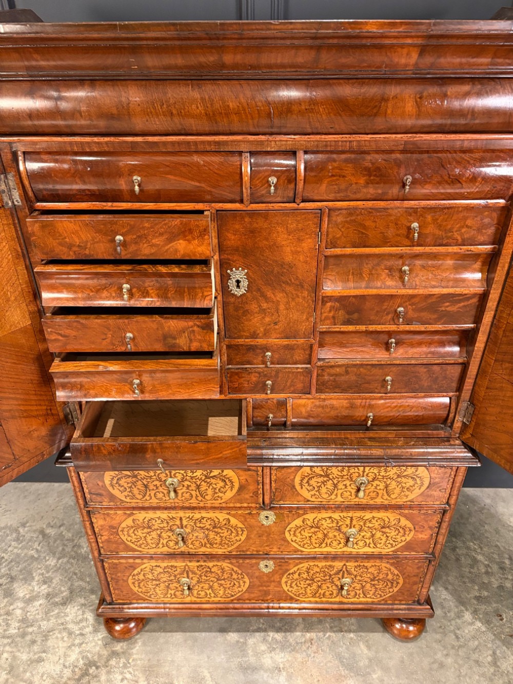 A William and Mary period burr walnut cabinet on stand featuring detailed floral marquetry inlays, teardrop brass handles, and heavy bun feet. View V