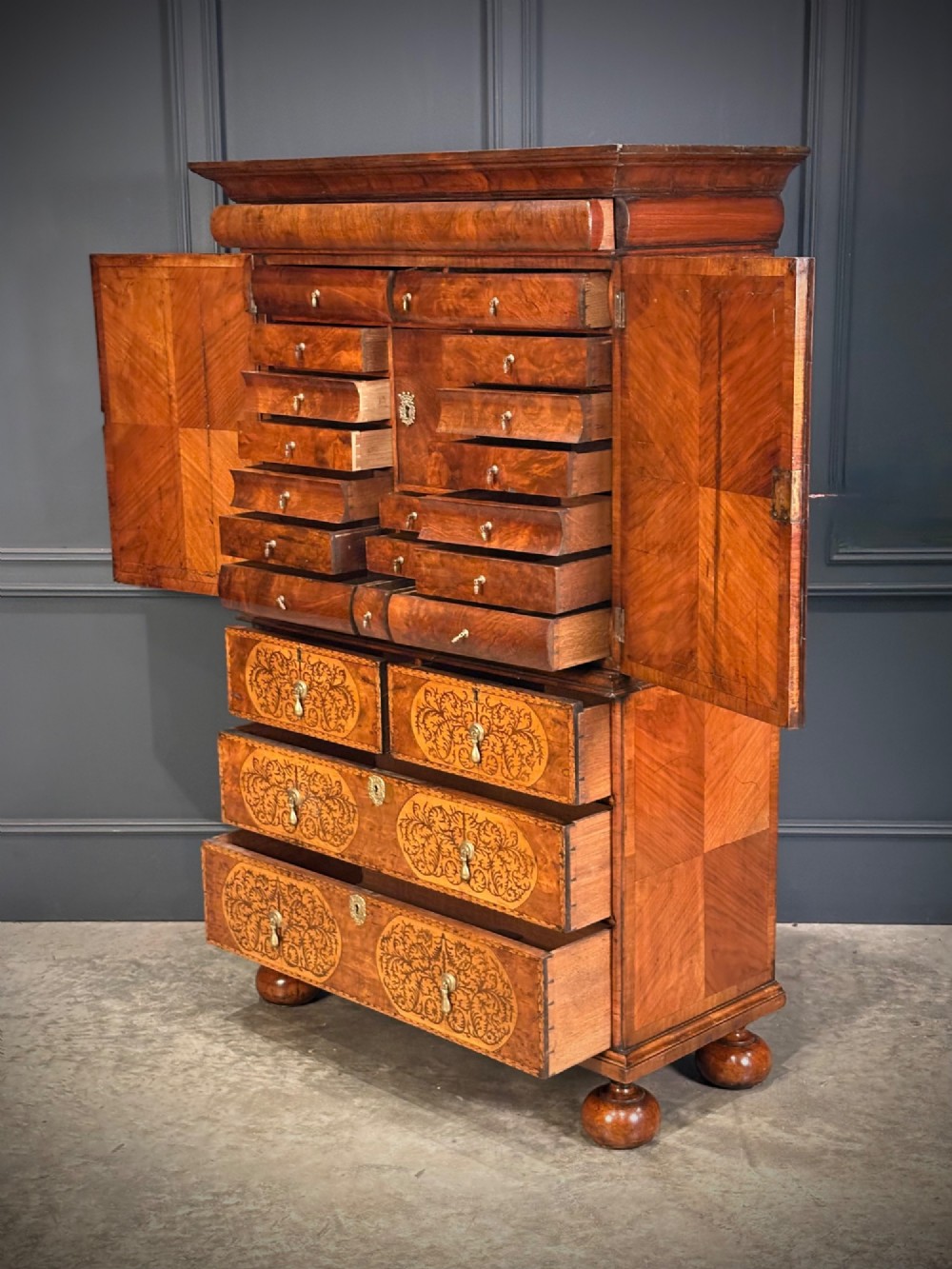 A William and Mary period burr walnut cabinet on stand featuring detailed floral marquetry inlays, teardrop brass handles, and heavy bun feet. View VII