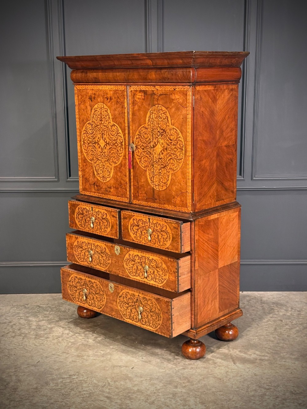 A William and Mary period burr walnut cabinet on stand featuring detailed floral marquetry inlays, teardrop brass handles, and heavy bun feet. View VIII