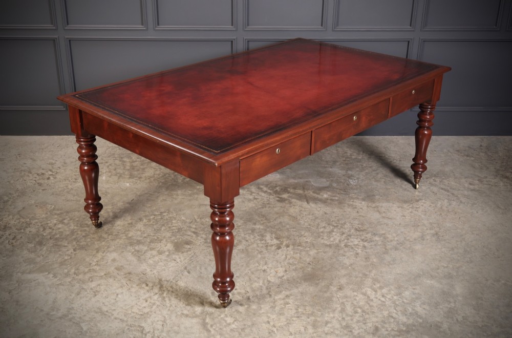 An early Victorian mahogany partners writing table featuring a red leather insert with gilt tooling, frieze drawers, turned legs, and brass castors.