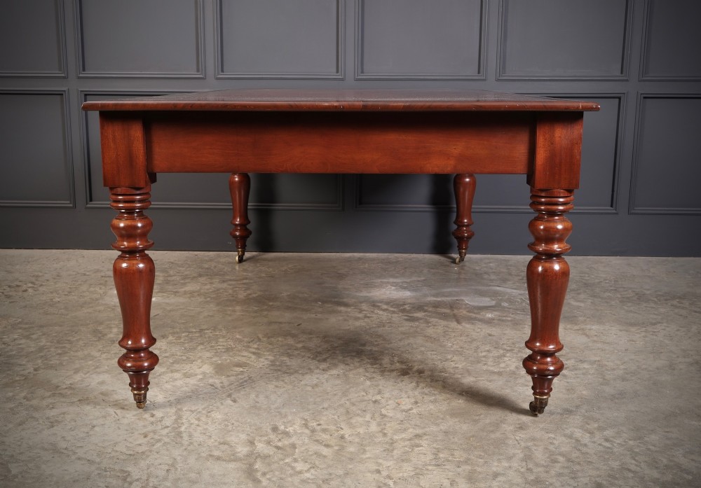 An early Victorian mahogany partners writing table featuring a red leather insert with gilt tooling, frieze drawers, turned legs, and brass castors. View VII