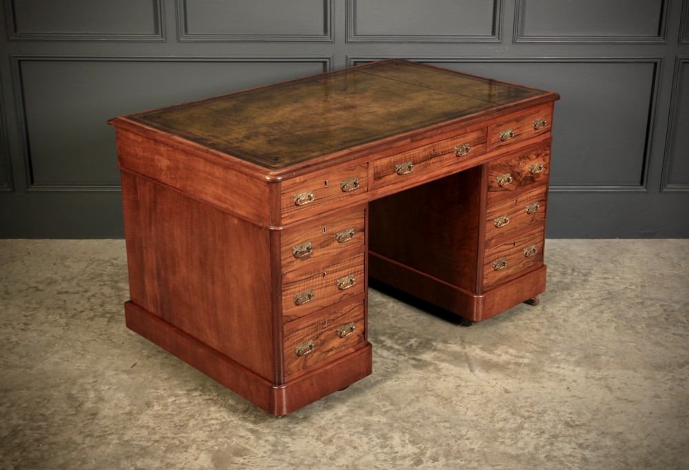 A Victorian walnut pedestal desk featuring a green leather inset top and multiple drawers with brass handles.