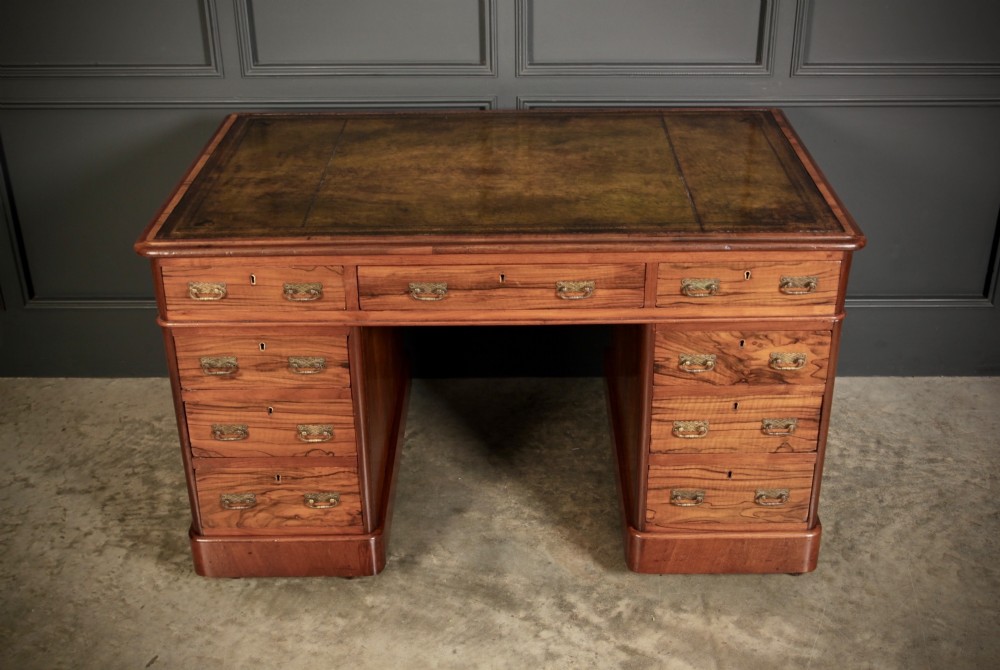 A Victorian walnut pedestal desk featuring a green leather inset top and multiple drawers with brass handles. View V