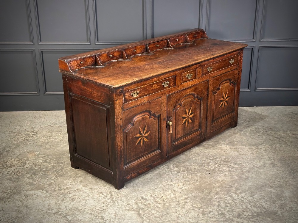 An 18th-century dark oak dresser base featuring three main drawers over three arched cupboard doors with star inlay details and brass handles. View II