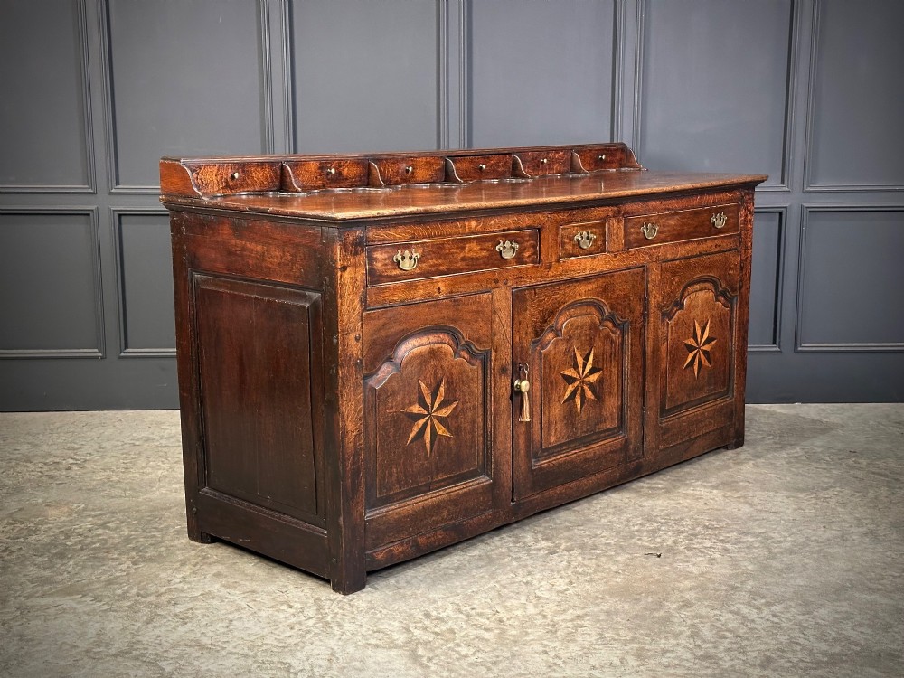 An 18th-century dark oak dresser base featuring three main drawers over three arched cupboard doors with star inlay details and brass handles. View III