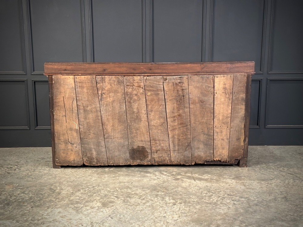 An 18th-century dark oak dresser base featuring three main drawers over three arched cupboard doors with star inlay details and brass handles. View X