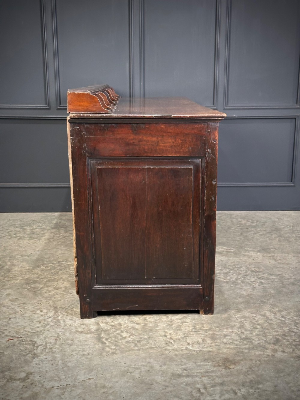 An 18th-century dark oak dresser base featuring three main drawers over three arched cupboard doors with star inlay details and brass handles. View XI