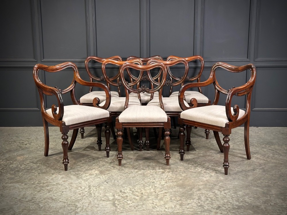 A set of eight Victorian rosewood dining chairs with balloon backs, carved details, scroll armrests, and neutral beige seats.