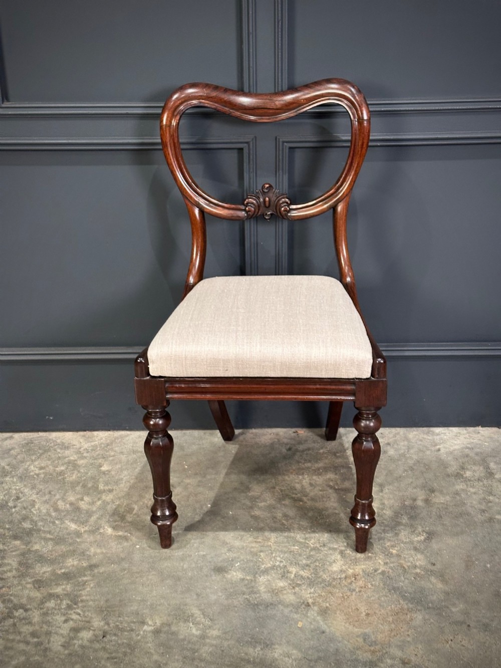 A set of eight Victorian rosewood dining chairs with balloon backs, carved details, scroll armrests, and neutral beige seats. View VI