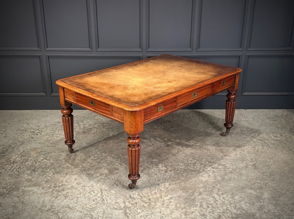 A large Victorian mahogany partners writing table featuring a tan leather writing top, flush brass handles, and fluted turned legs on brass castors. View II