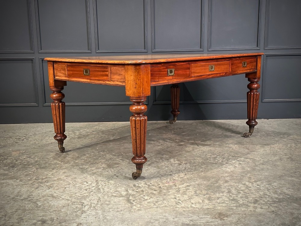 A large Victorian mahogany partners writing table featuring a tan leather writing top, flush brass handles, and fluted turned legs on brass castors. View III