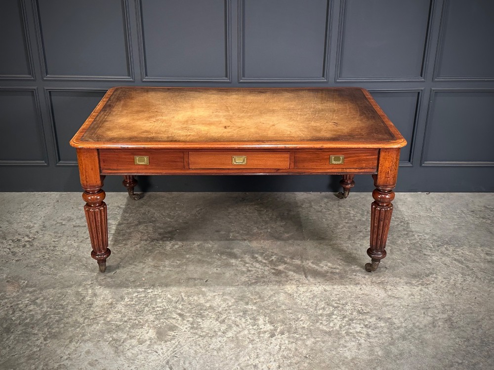 A large Victorian mahogany partners writing table featuring a tan leather writing top, flush brass handles, and fluted turned legs on brass castors. View IV