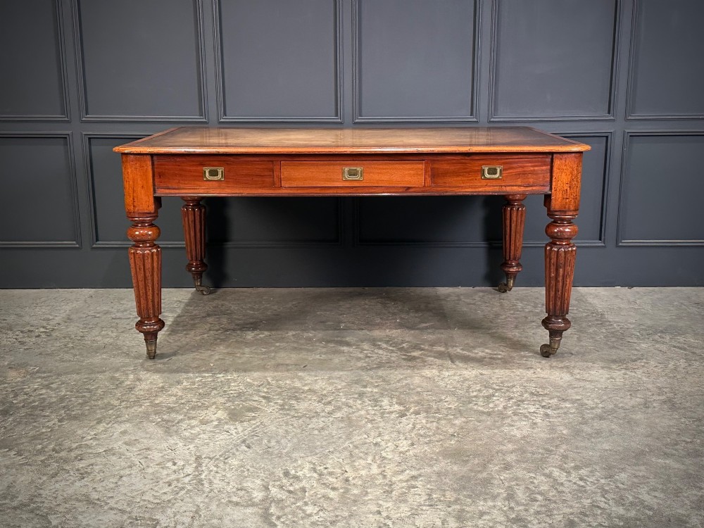 A large Victorian mahogany partners writing table featuring a tan leather writing top, flush brass handles, and fluted turned legs on brass castors. View V