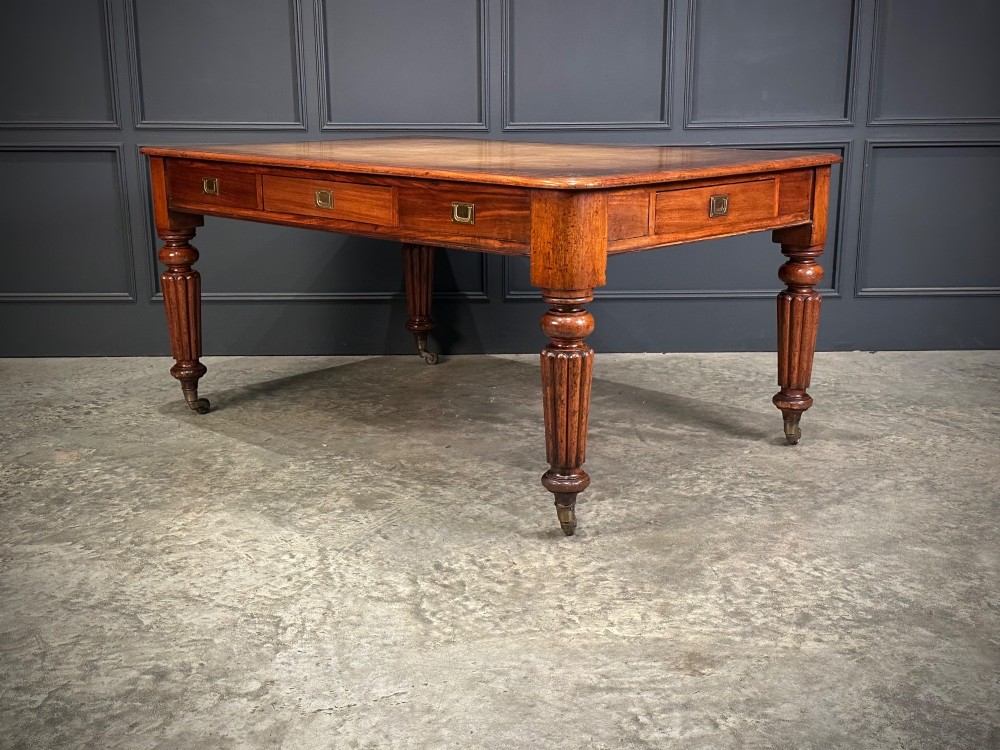 A large Victorian mahogany partners writing table featuring a tan leather writing top, flush brass handles, and fluted turned legs on brass castors. View VI