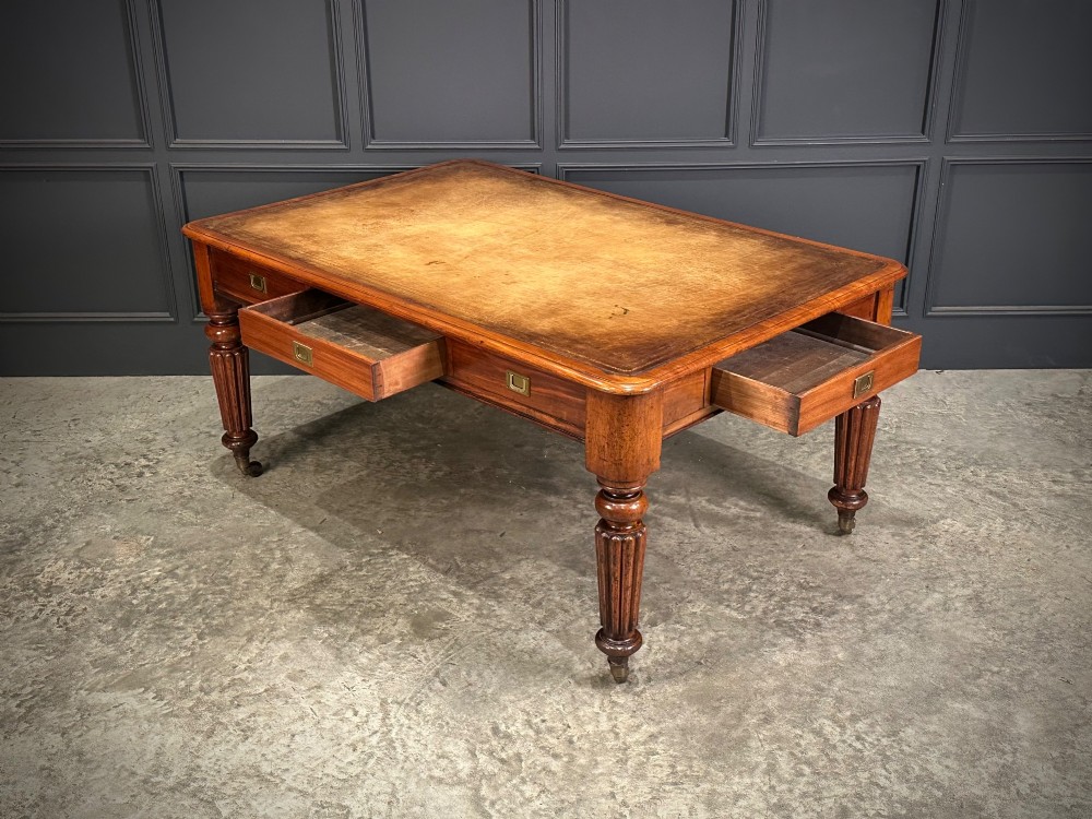 A large Victorian mahogany partners writing table featuring a tan leather writing top, flush brass handles, and fluted turned legs on brass castors. View VII