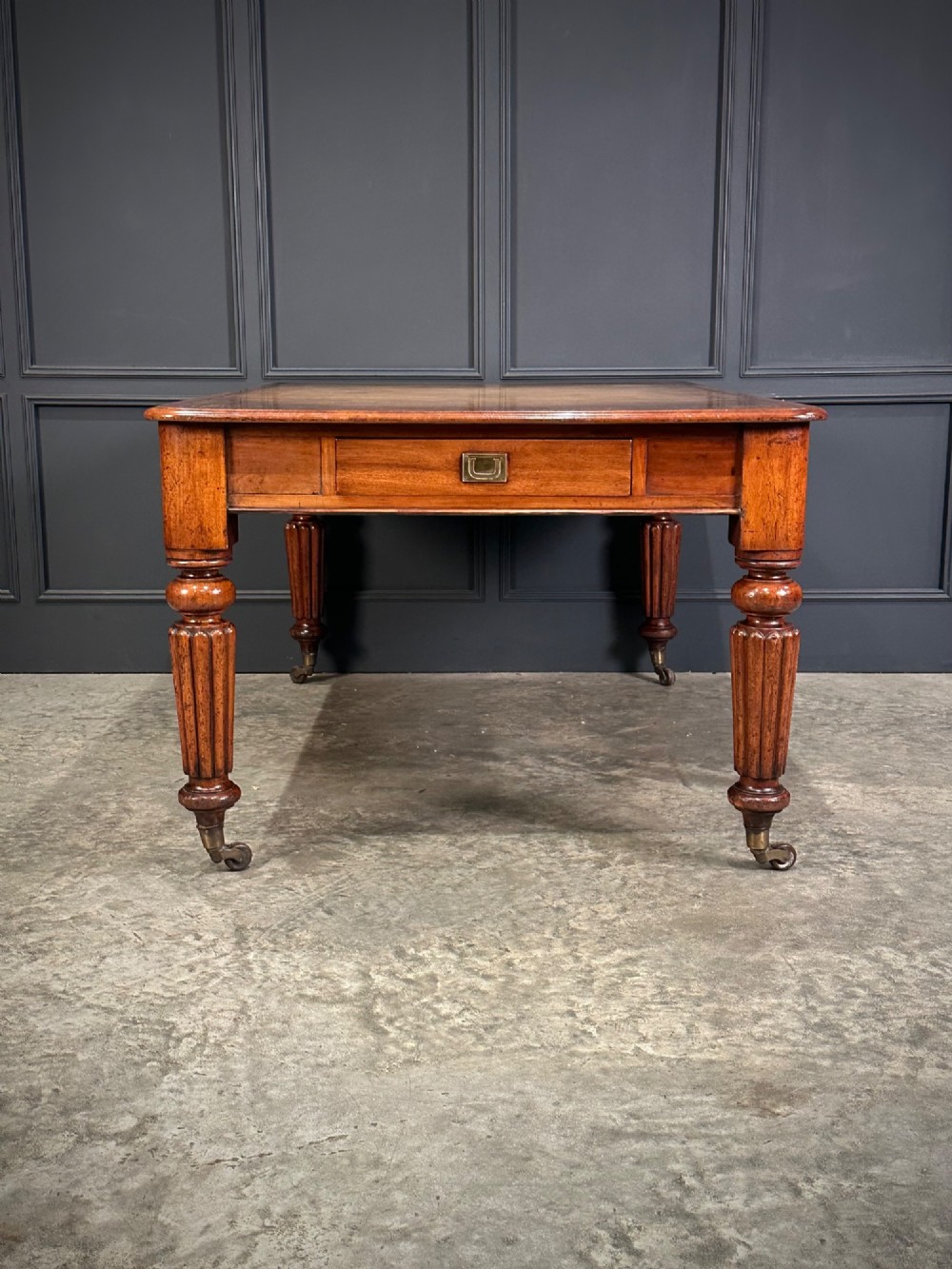 A large Victorian mahogany partners writing table featuring a tan leather writing top, flush brass handles, and fluted turned legs on brass castors. View VIII