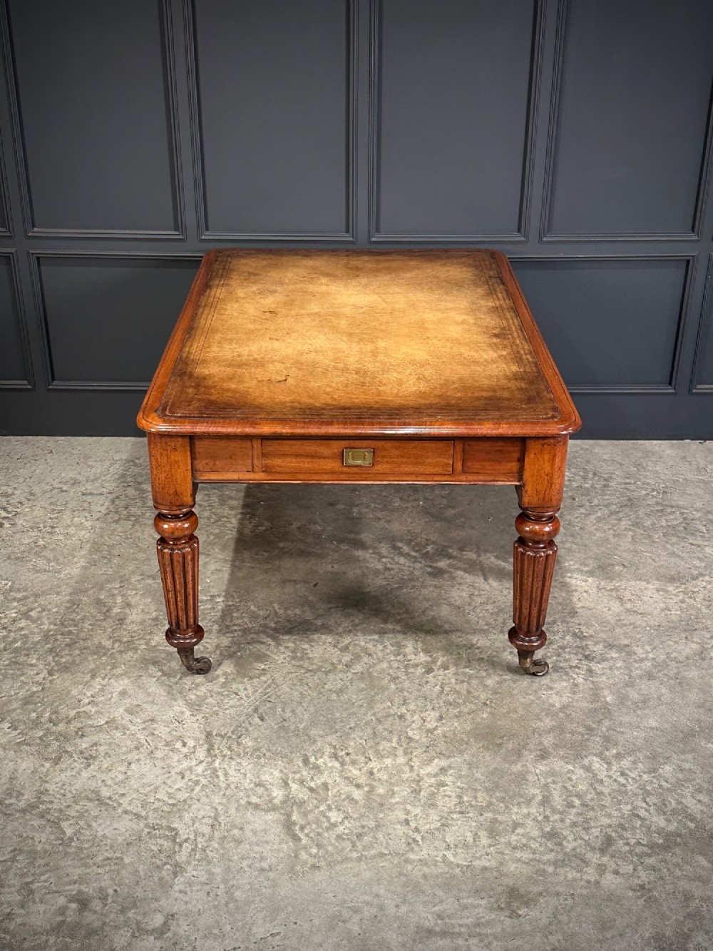 A large Victorian mahogany partners writing table featuring a tan leather writing top, flush brass handles, and fluted turned legs on brass castors. View IX