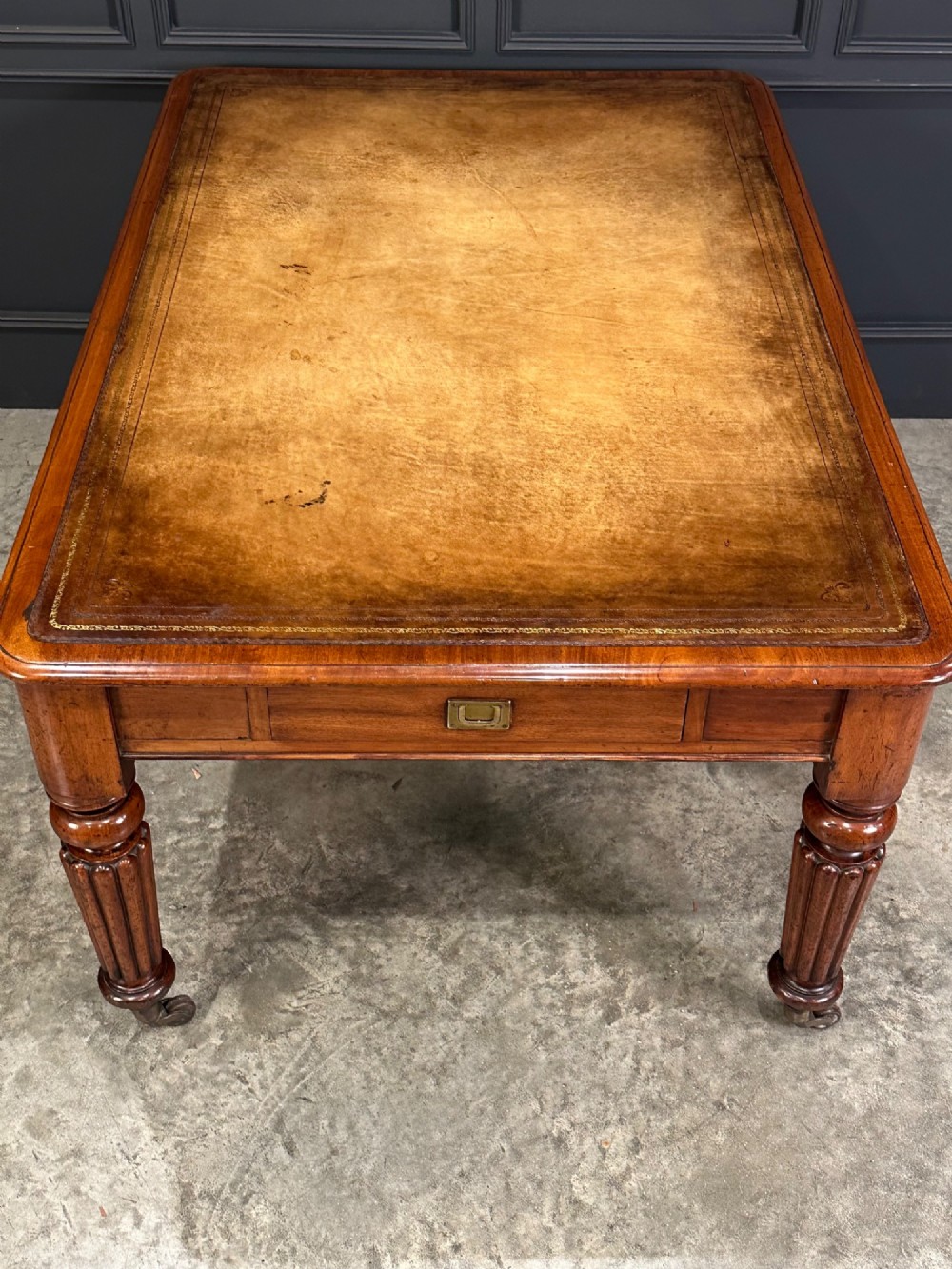 A large Victorian mahogany partners writing table featuring a tan leather writing top, flush brass handles, and fluted turned legs on brass castors. View X