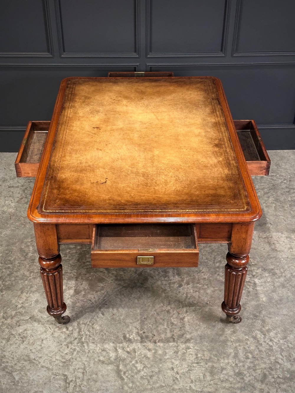 A large Victorian mahogany partners writing table featuring a tan leather writing top, flush brass handles, and fluted turned legs on brass castors. View XI