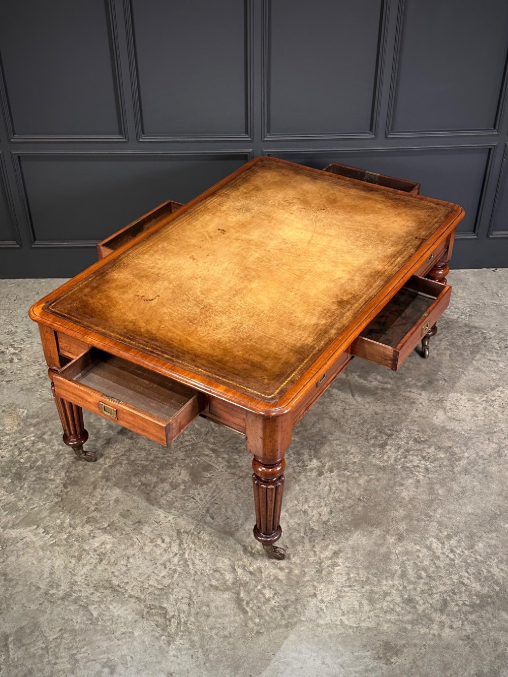 A large Victorian mahogany partners writing table featuring a tan leather writing top, flush brass handles, and fluted turned legs on brass castors. View XII