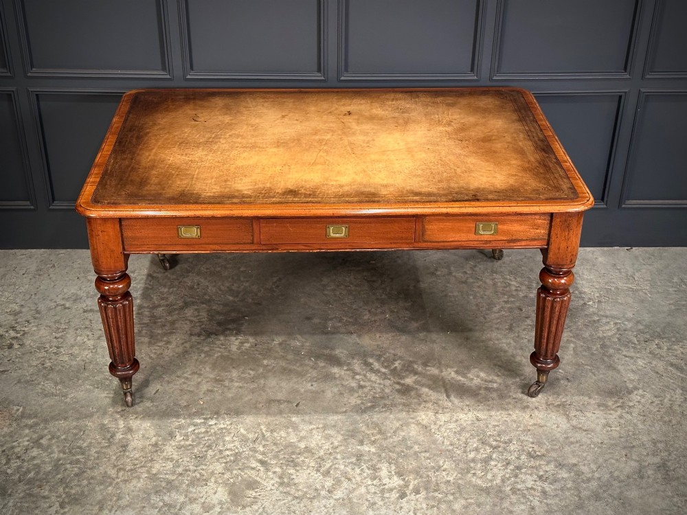 A large Victorian mahogany partners writing table featuring a tan leather writing top, flush brass handles, and fluted turned legs on brass castors. View XIII