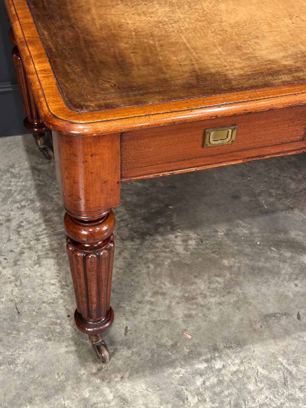 A large Victorian mahogany partners writing table featuring a tan leather writing top, flush brass handles, and fluted turned legs on brass castors. View XIV