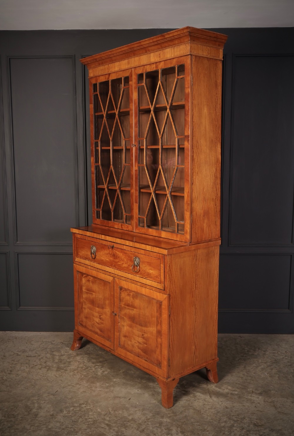 A tall Georgian satinwood secretaire bookcase featuring an upper glazed cabinet with geometric astragal bars, a fold-down desk drawer, and a lower double-door cupboard on splayed bracket feet. View VI