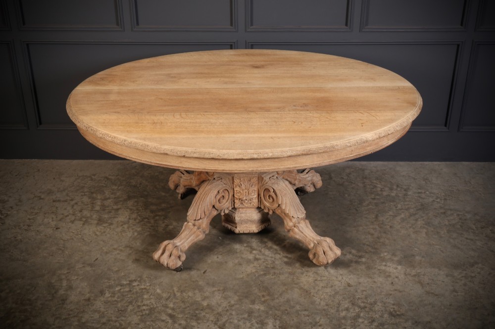 A circular bleached oak centre table featuring a carved central column and four scroll legs with carved paw feet.