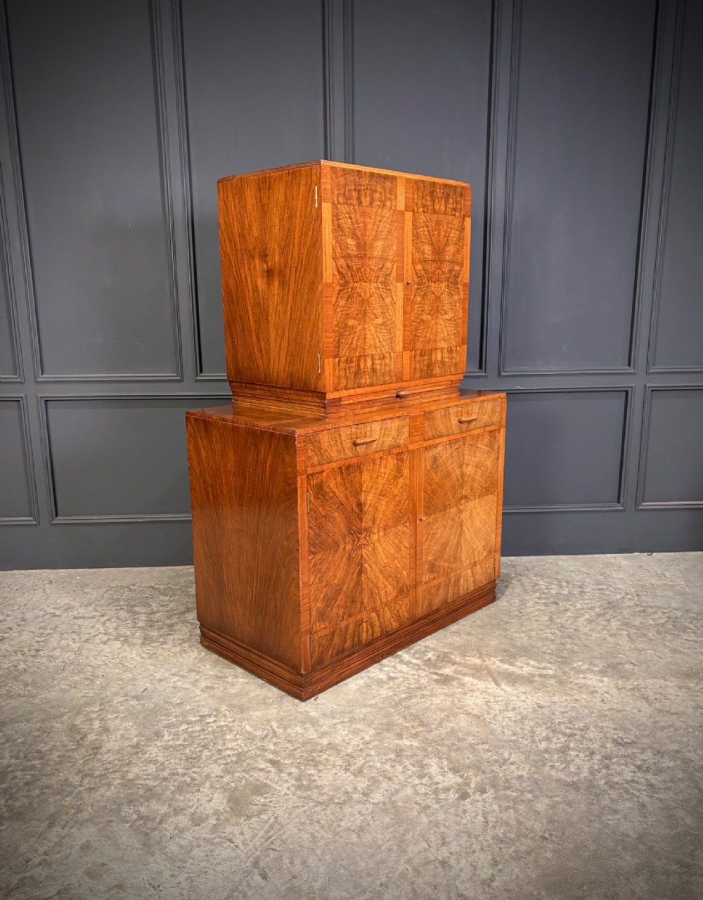 An Art Deco two-tiered cocktail cabinet in figured walnut veneer featuring double doors and geometric paneling.