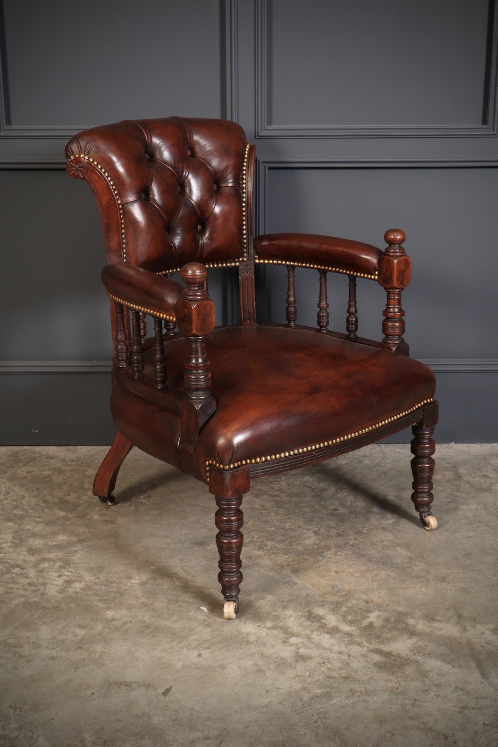 Pair of Victorian mahogany desk chairs with buttoned chestnut brown leather upholstery, brass studding, turned spindles, and castors. View III