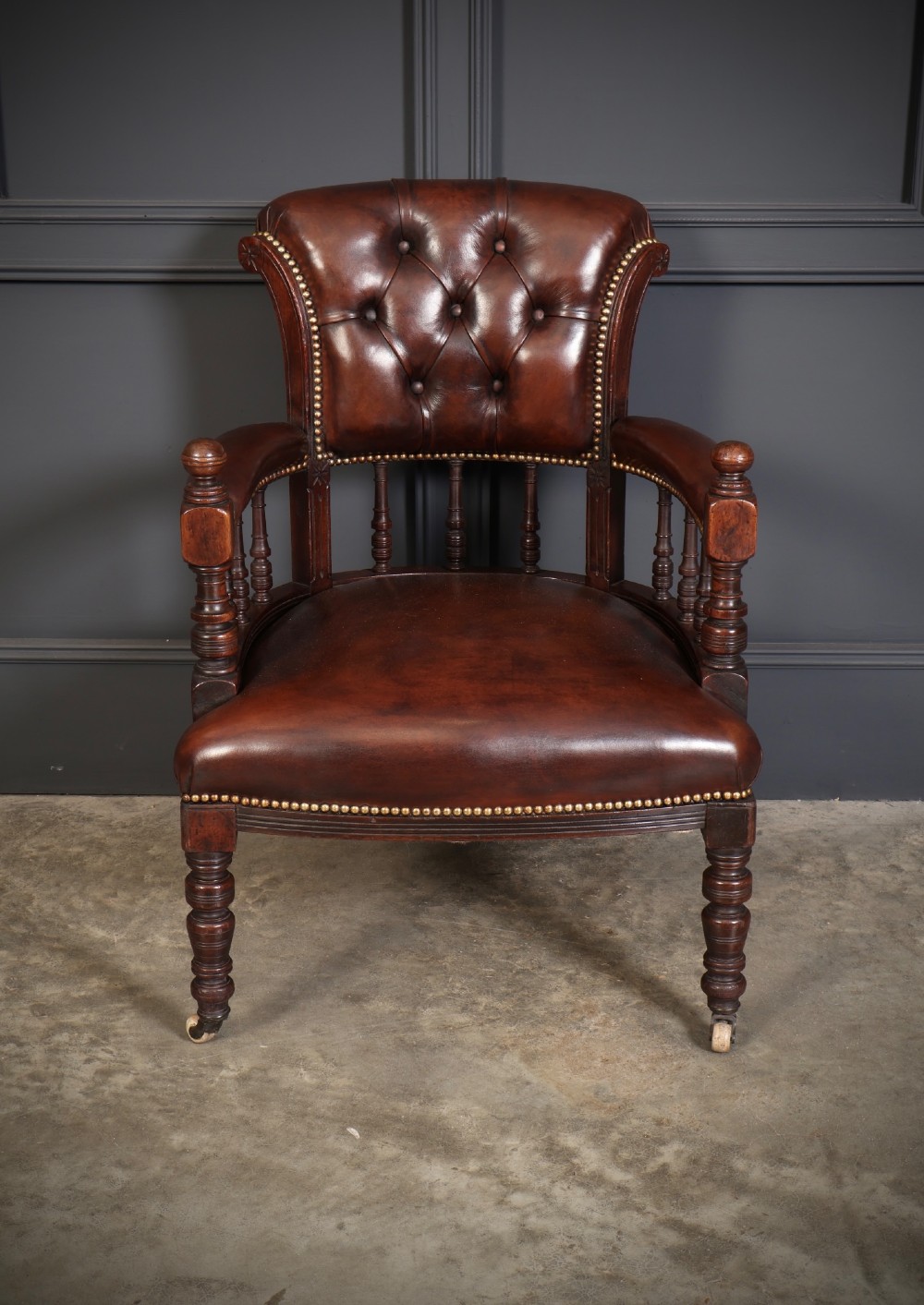 Pair of Victorian mahogany desk chairs with buttoned chestnut brown leather upholstery, brass studding, turned spindles, and castors. View V